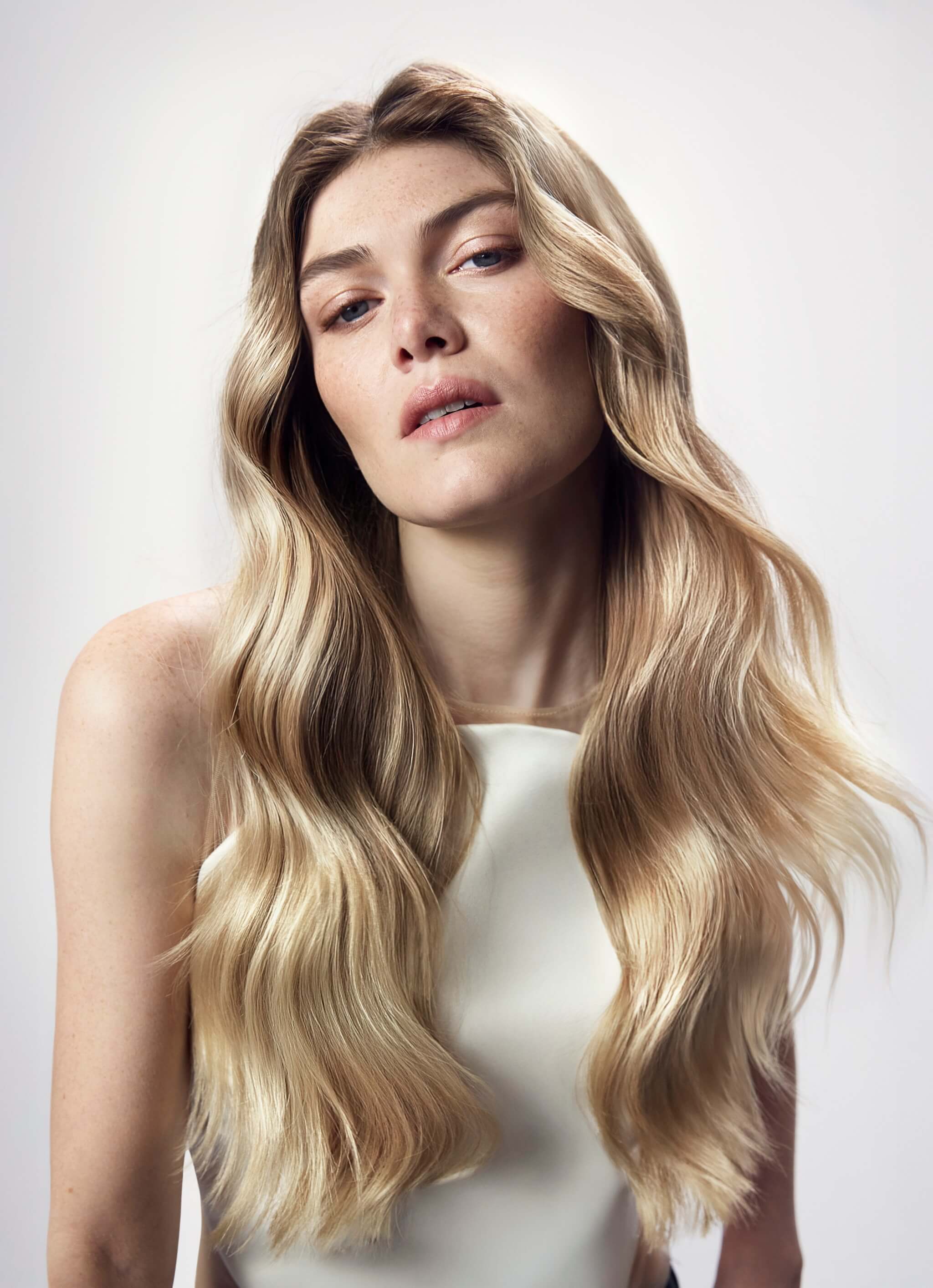 Woman with long, wavy blonde hair against a plain background