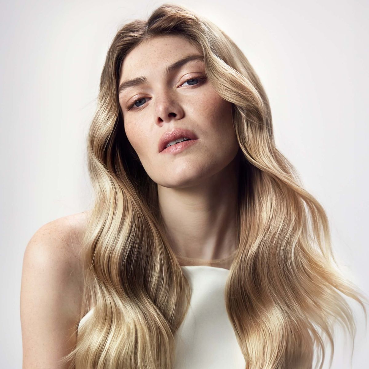 Woman with long, wavy blonde hair against a plain background